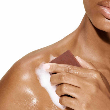 Image of a female model using a bar of Antü Restoring Soap on her shoulder.