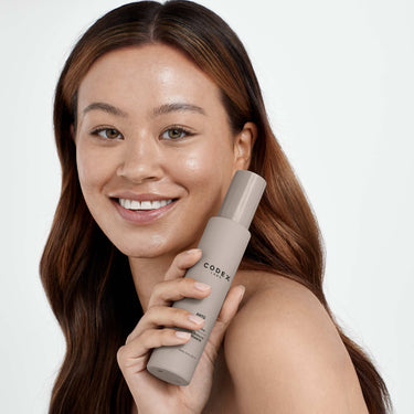 Woman smiling holding a bottle of Antü Radiance Mist.